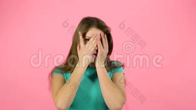 小女孩害怕，把她的脸藏在粉红背景的工作室里。